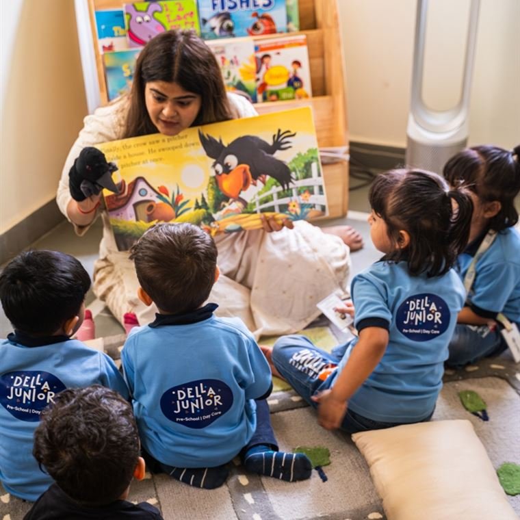 A Della Junior teacher reading a picture book with a puppet to her class