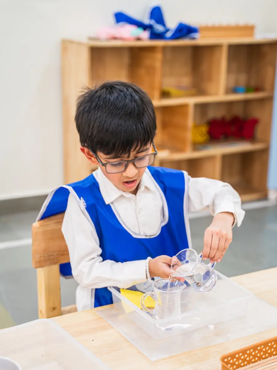 A boy carefully pouring water from one jug into another