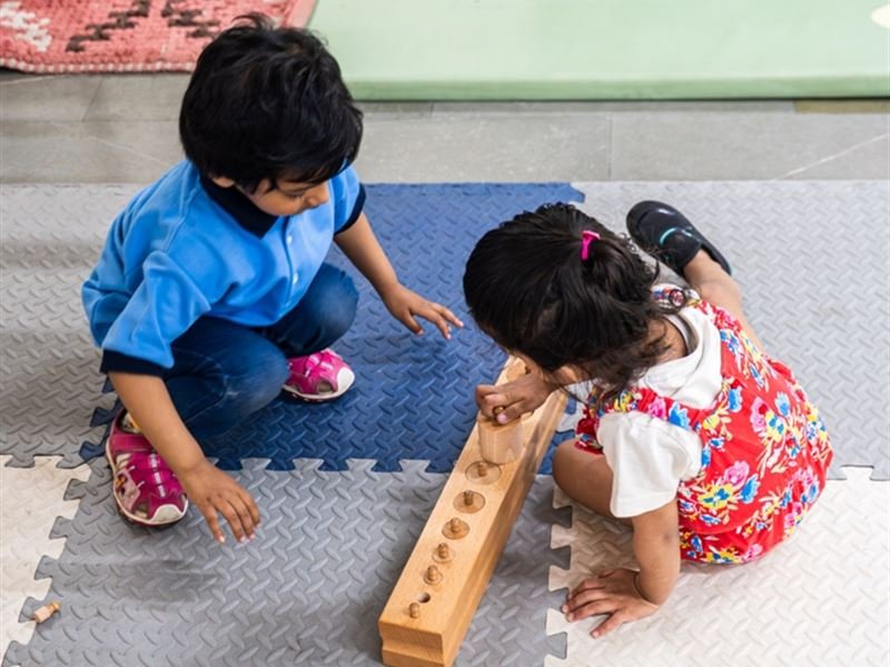 Two children exploring a wooden cylinder block together