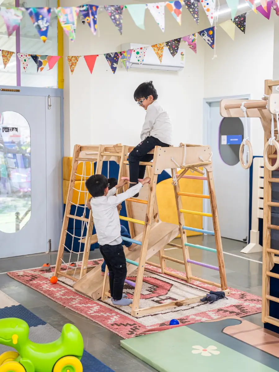 Children climbing a wooden climbing frame indoors
