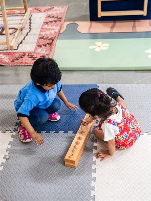 Two children exploring a wooden cylinder block together