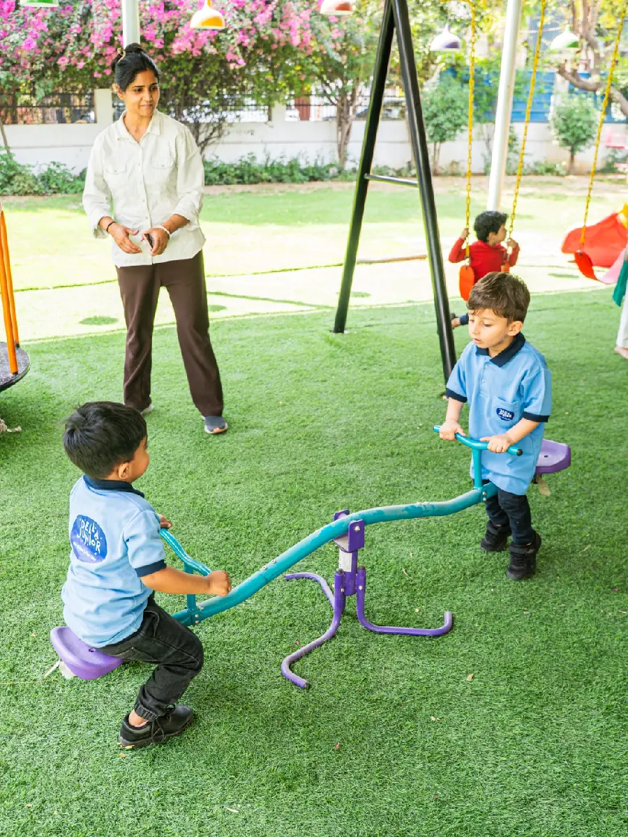 Two boys sharing a seesaw while their teacher looks on